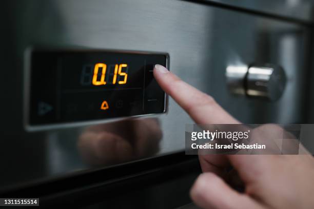 close-up of a caucasian woman's finger pressing the oven controls. she is ready to cook - timer stock-fotos und bilder