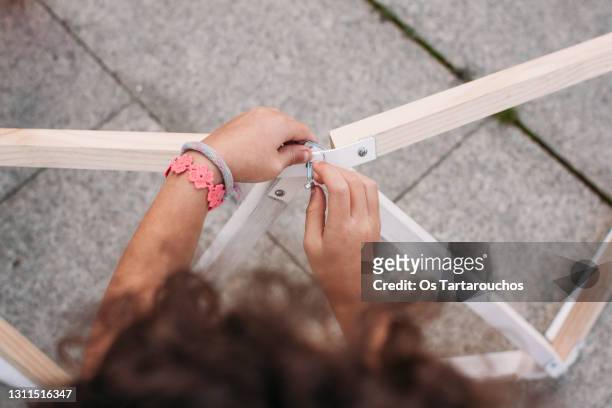 girl's hands assembling a wooden and metal frame with a screw and a nut - bracelet fotografías e imágenes de stock