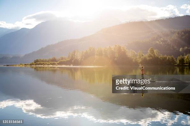 woman paddleboarding on calm lake in whistler during sunrise. - lake sunrise stock pictures, royalty-free photos & images