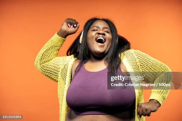 portrait of dancing young woman standing against orange background - fat woman dancing stockfoto's en -beelden
