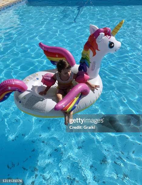 a child on a unicorn float in the pool - schwimmhilfe stock-fotos und bilder