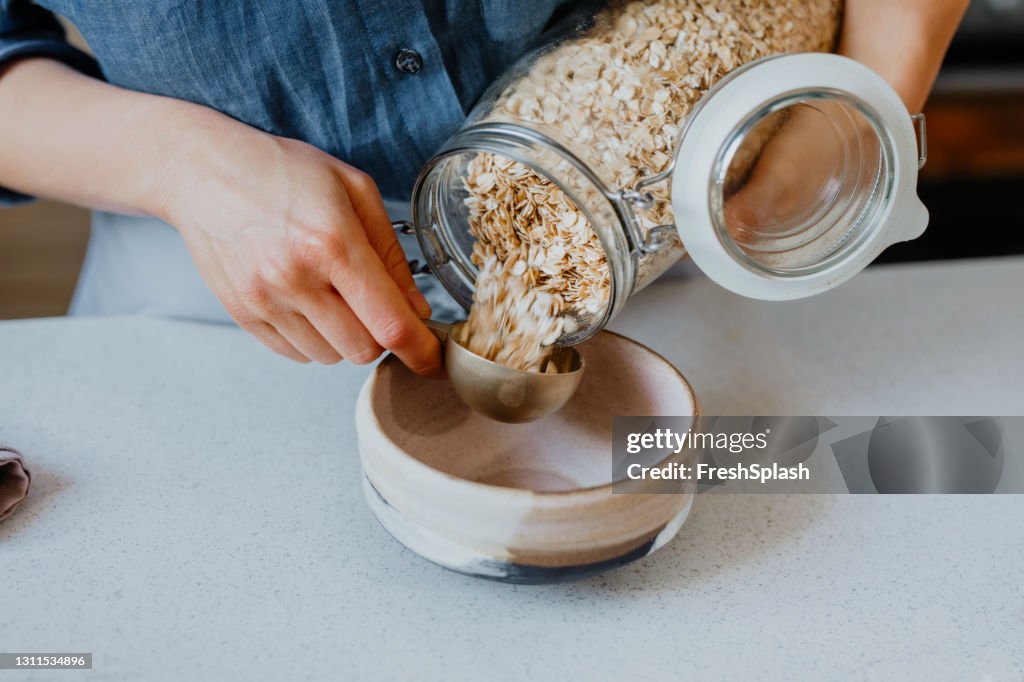 Making Breakfast: Hände einer Frau, die gerollten Hafer in eine Schüssel steckt