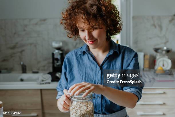 ein gesundes und nahrhaftes frühstück machen: frau öffnet ein glas gerollten hafer - rolled oats stock-fotos und bilder