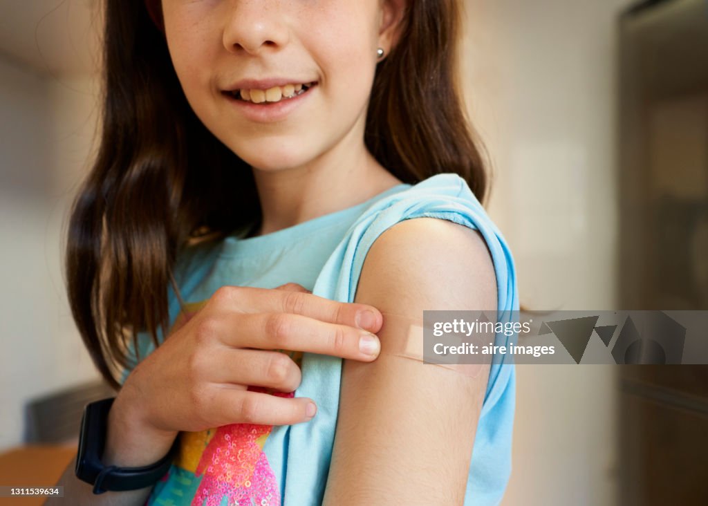 Girl looking at camera pointing at her arm with a bandage after getting the covid-19 vaccine.