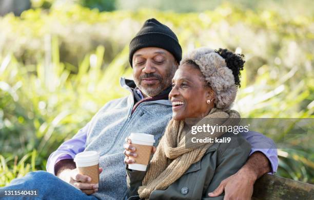 afroamerikanische entspannung auf parkbank trinken kaffee - candid mature couple outdoors stock-fotos und bilder
