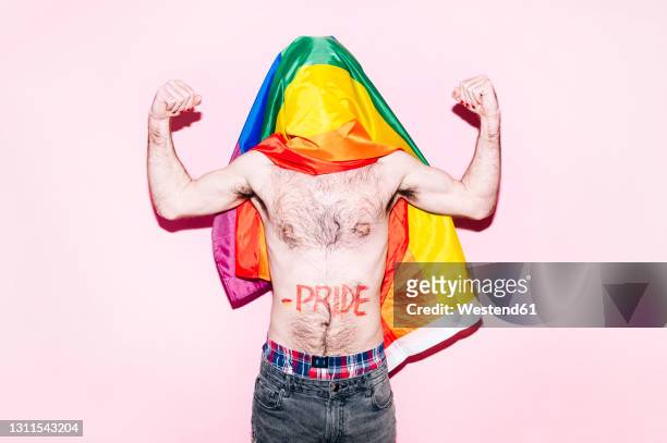 covered face of gay man with rainbow flag flexing biceps standing against pink background - hairy man stockfoto's en -beelden