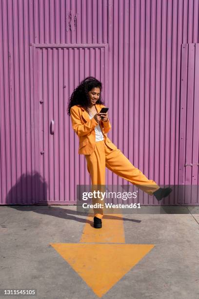 young woman using phone while standing on footpath - purple suit fotografías e imágenes de stock