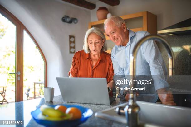 spanish senior couple using laptop in kitchen - pensioners demonstrate in spain stock pictures, royalty-free photos & images