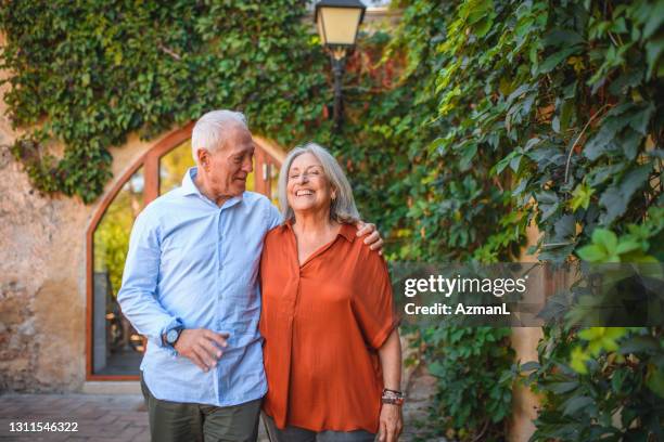 candid portrait of smiling senior couple walking outdoors - man talking to camera stock pictures, royalty-free photos & images