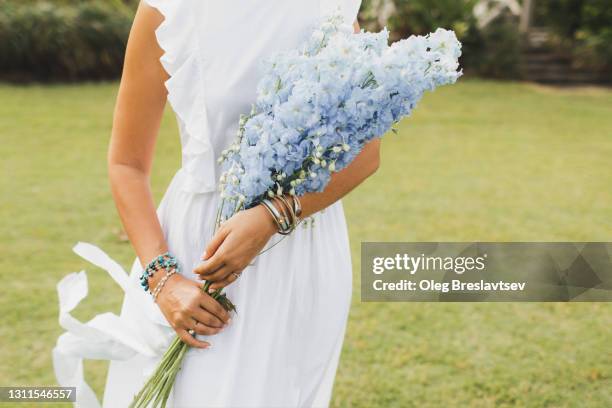 bouquet of blue delphinium flowers in bride's hands close-up. bijouterie bracelets on hands - bridal styles stock-fotos und bilder