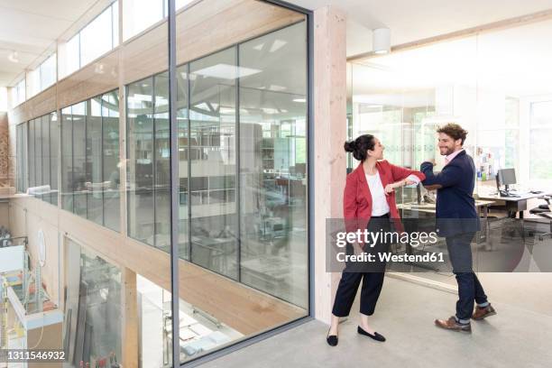 smiling male and female entrepreneurs giving elbow bump at office - ellenbogengruß stock-fotos und bilder