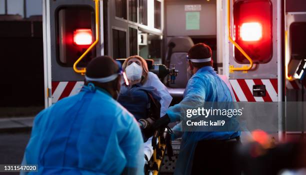 paramedics loading patient into ambulance, wearing ppe - urgent care stock pictures, royalty-free photos & images