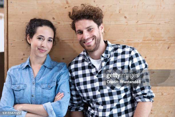 smiling male and female entrepreneurs against wooden wall - curly hair woman white shirt stock pictures, royalty-free photos & images