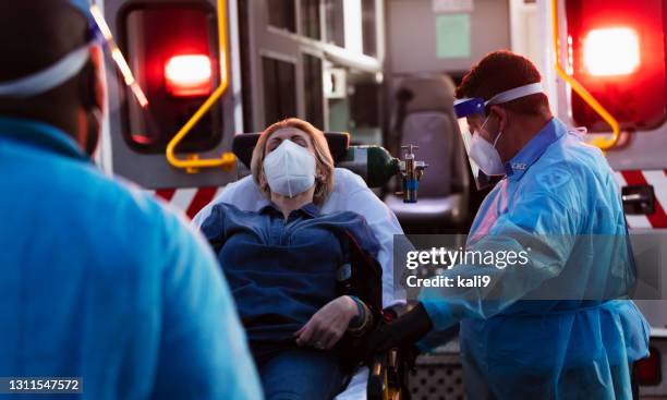 paramedics loading patient into ambulance, wearing ppe - ambulance lights stock pictures, royalty-free photos & images