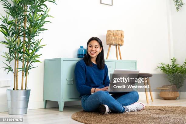 smiling young woman sitting with laptop on jute rug at home - chinese student laptop stock pictures, royalty-free photos & images