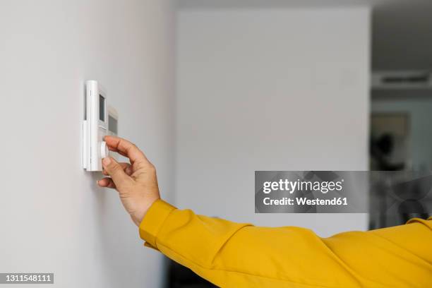 mature woman adjusting thermostat in living room - thermostat fotografías e imágenes de stock