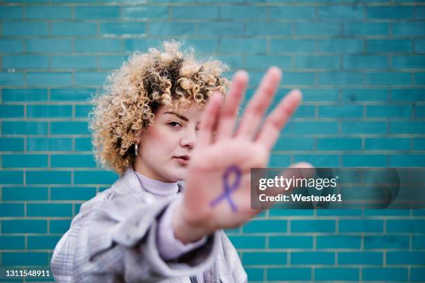 curly haired woman showing colon cancer ribbon symbol on hand - colorectal cancer stockfoto's en -beelden