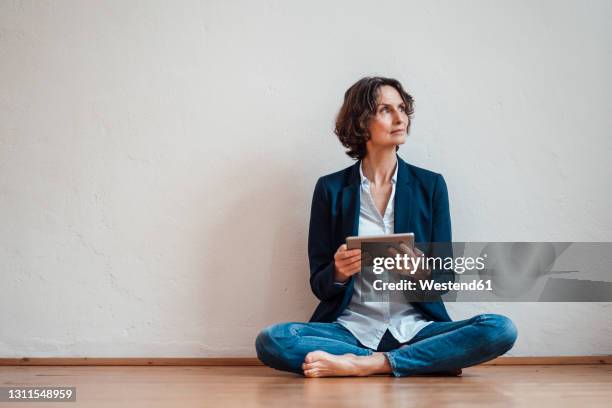 thoughtful businesswoman with digital tablet sitting on floor in front of white wall - sitting on ground stock pictures, royalty-free photos & images
