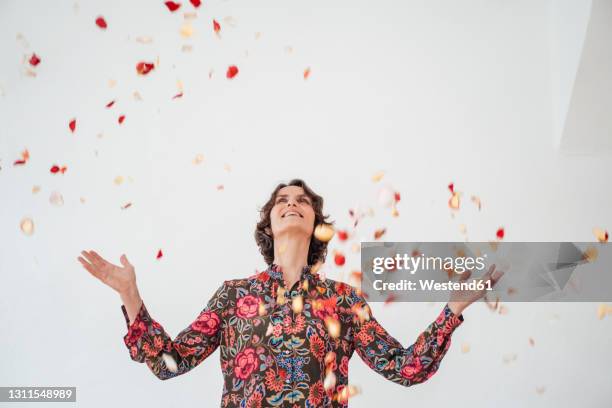 cheerful woman throwing confetti in front of white wall - throwing flowers stock pictures, royalty-free photos & images