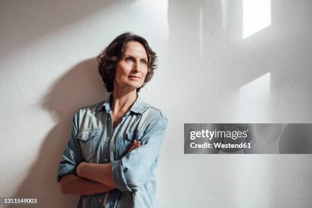 confident woman with arms crossed looking away during sunny day - older woman with brown hair stockfoto's en -beelden