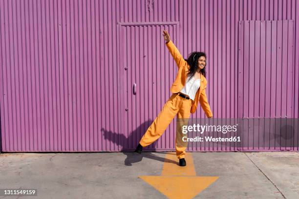 happy young woman wearing headphones while dancing on footpath - metallic suit stock pictures, royalty-free photos & images