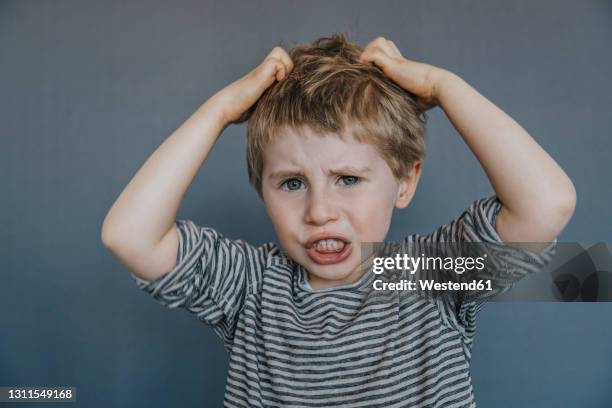 frustrated boy scratching head against gray background - scratching head stock pictures, royalty-free photos & images