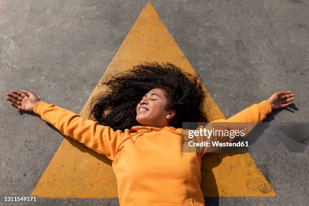 carefree young woman with eyes closed lying down on footpath - curly arrow stock pictures, royalty-free photos & images