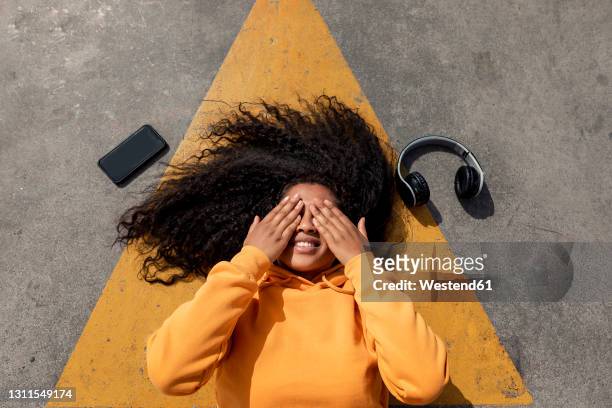 young woman covering eyes while lying down on footpath - curly arrow stock pictures, royalty-free photos & images