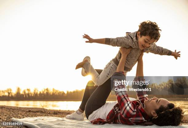 young woman picking up boy with arms outstretched while playing during sunset - pretending to be a plane stock pictures, royalty-free photos & images