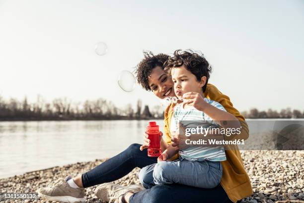 boy playing with bubble wand while sitting on mother's lap during sunny day - 5 loch stock pictures, royalty-free photos & images