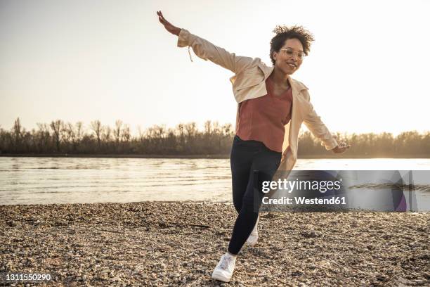happy woman with arms outstretched running by lake - 飛行機のまね ストックフォトと画像