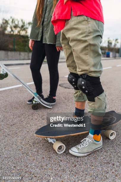 woman with skateboard wearing protective kneepad while standing by female friend on road - kneepad stock pictures, royalty-free photos & images