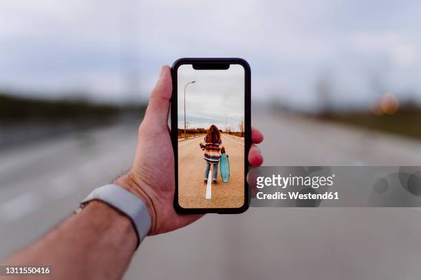 man photographing woman with skateboard standing on road - femme de dos smartphone photos et images de collection