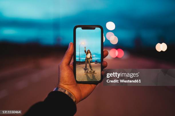 young man photographing woman on skateboard during dusk - smartphone pov stockfoto's en -beelden