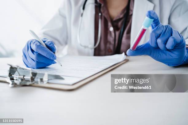 female doctor holding blood sample while writing medical report at desk - blood collection tube stock-fotos und bilder