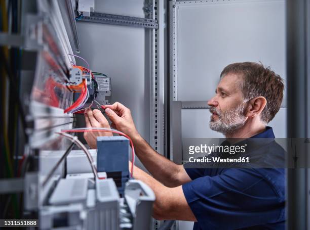 male electrician examining power supply in electrical workshop - electromonteur stock-fotos und bilder