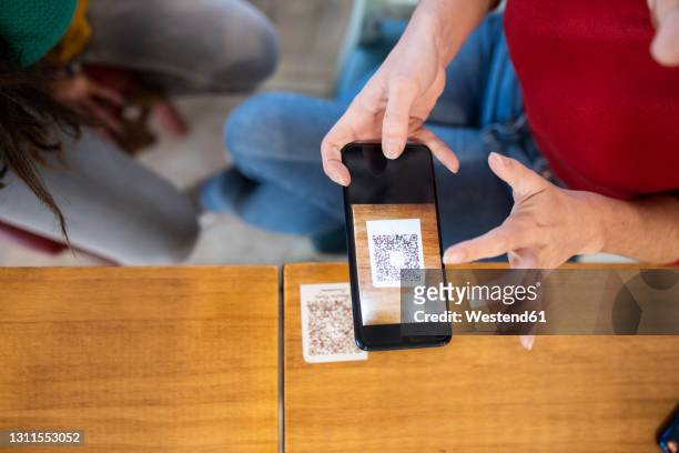 woman scanning qr code through smart phone at cafe - qrコード ストックフォトと画像