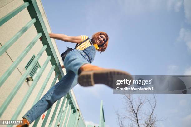 young woman balancing on railing against sky - low angle view stock-fotos und bilder