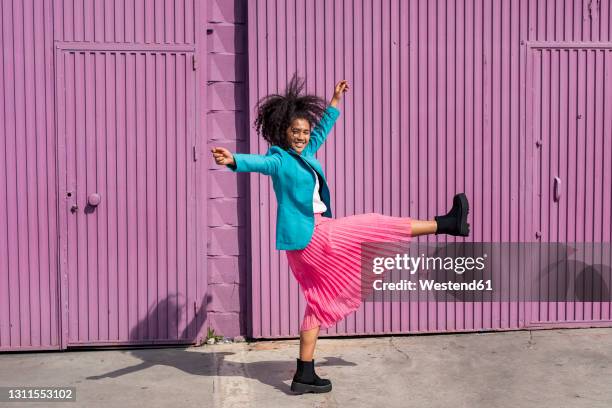 carefree young woman dancing in front of purple cabin - tossing hair facing camera woman outdoors stock-fotos und bilder