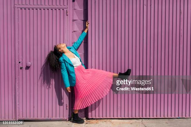 young woman dancing by purple cabin on sunny day - purple coat fotografías e imágenes de stock