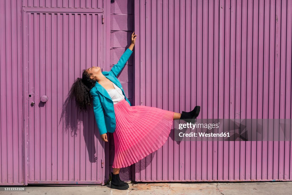 Young woman dancing by purple cabin on sunny day
