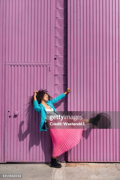 playful young woman dancing by purple cabin wall on sunny day - blazer viola foto e immagini stock