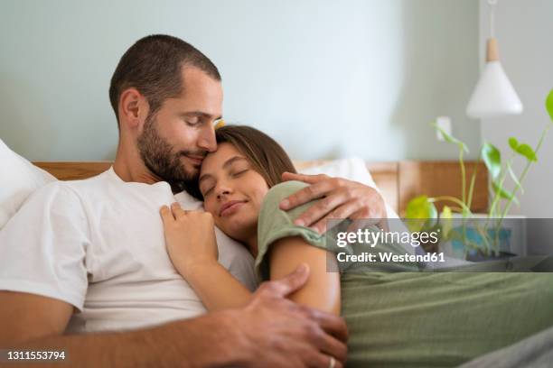 young couple relaxing while lying on bed at home - paar kuscheln bett stock-fotos und bilder