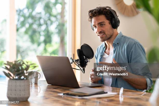 male freelancer speaking on microphone while recording podcast at home - podcasting stock-fotos und bilder