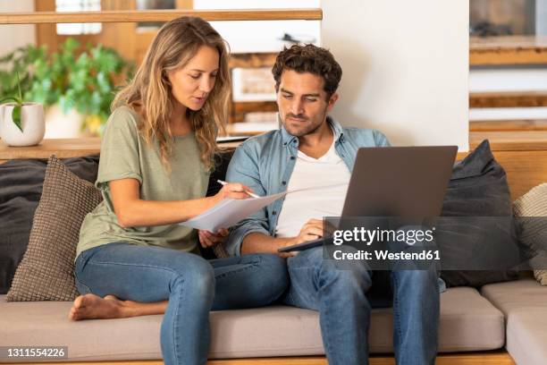 girlfriend signing papers by man with laptop sitting on couch at home - man signing paper stock pictures, royalty-free photos & images