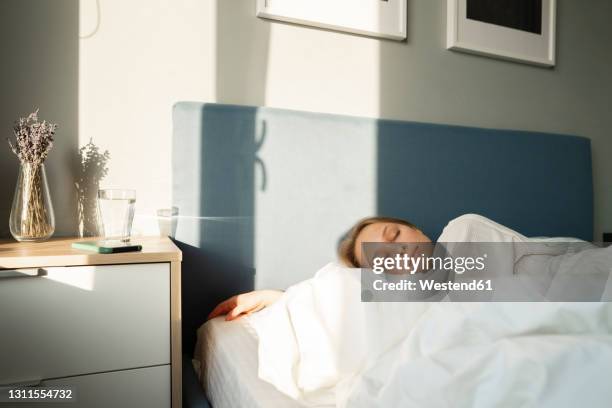young woman sleeping in bed by table at home - acostado de lado fotografías e imágenes de stock