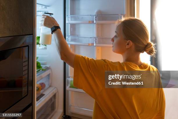 woman putting milk bottle in fridge at home - milk bottle photos et images de collection