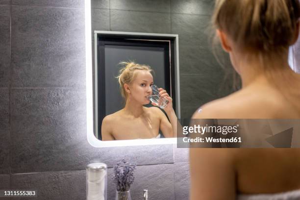 reflection of woman drinking water in bathroom - mouthwash stock-fotos und bilder