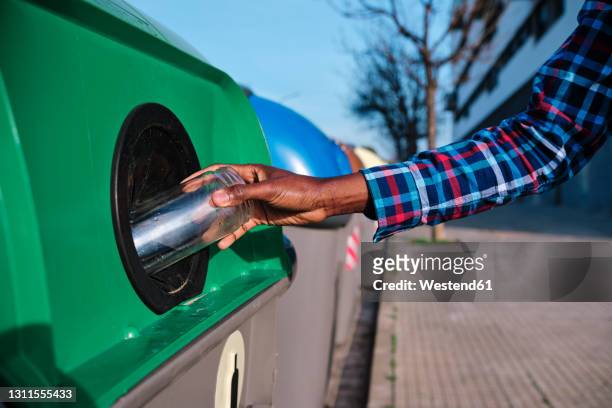 man putting glass jar in recycling bin on footpath - glasbak stockfoto's en -beelden