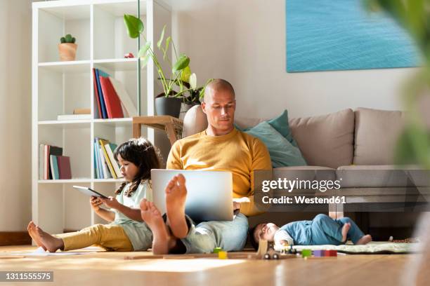 father working on laptop while sitting by daughters at home - familie laptop stock-fotos und bilder